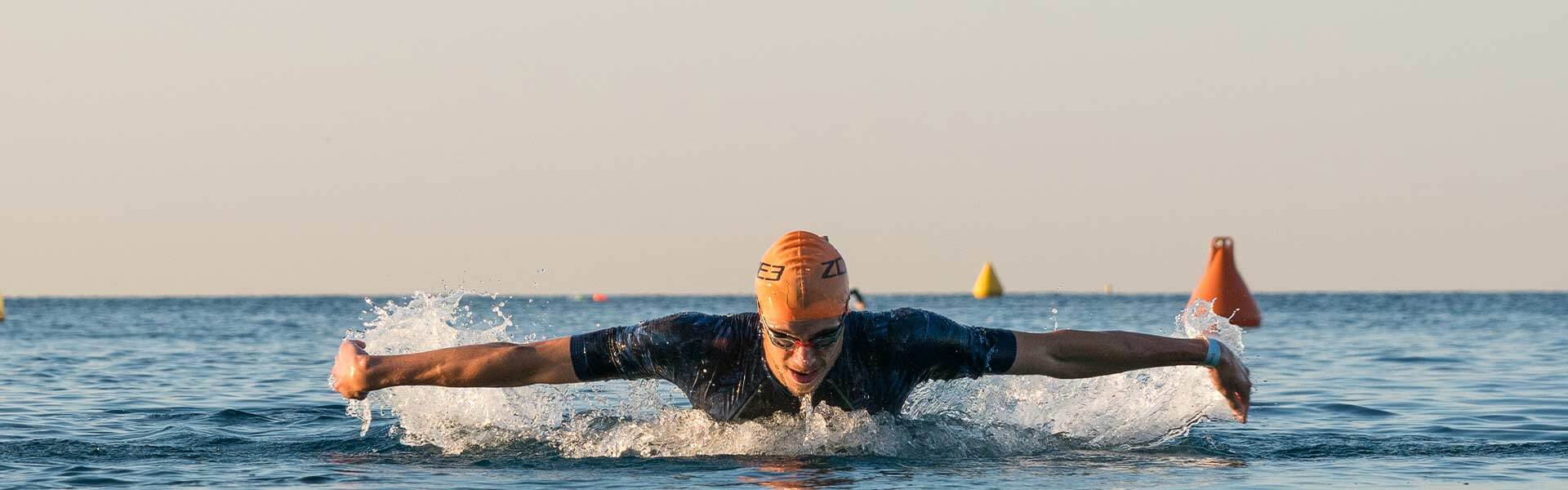 Swimmer in orange cap gliding through open water with buoys in the distance.