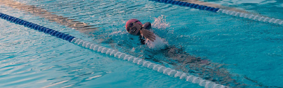 Swimmer in pink cap glides through blue pool water during a sprint triathlon training lap.