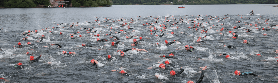 Large group of swimmers wearing red caps race in open water.