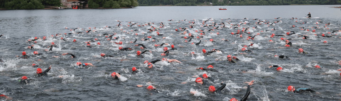 Large group of swimmers wearing red caps race in open water.