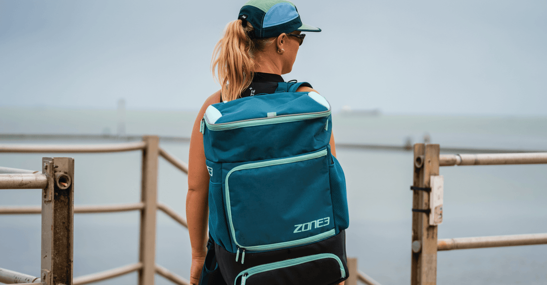 Back view of a cyclist wearing a teal backpack along a coastal road