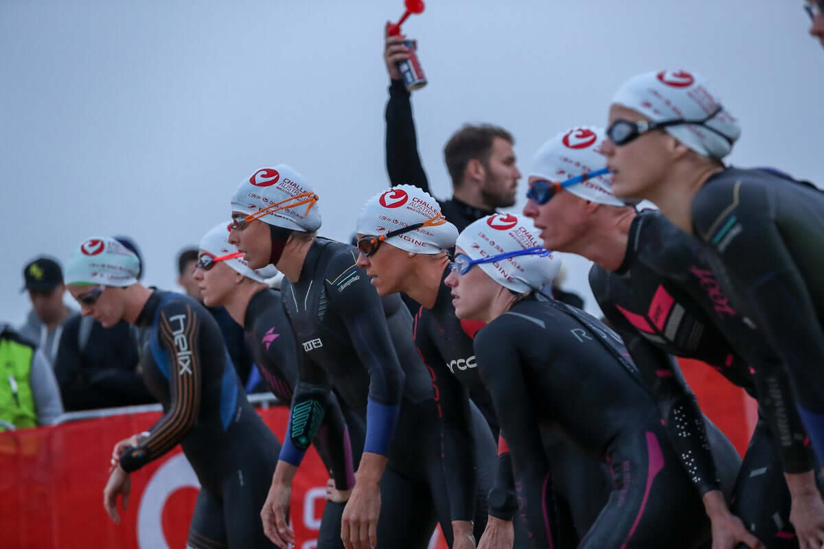 Triathletes in wetsuits and white swim caps riding in a peloton at Challenge Melbourne