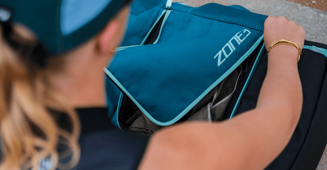 Close up of a teal Zone3 waterproof transition bag being opened on a cyclist's back