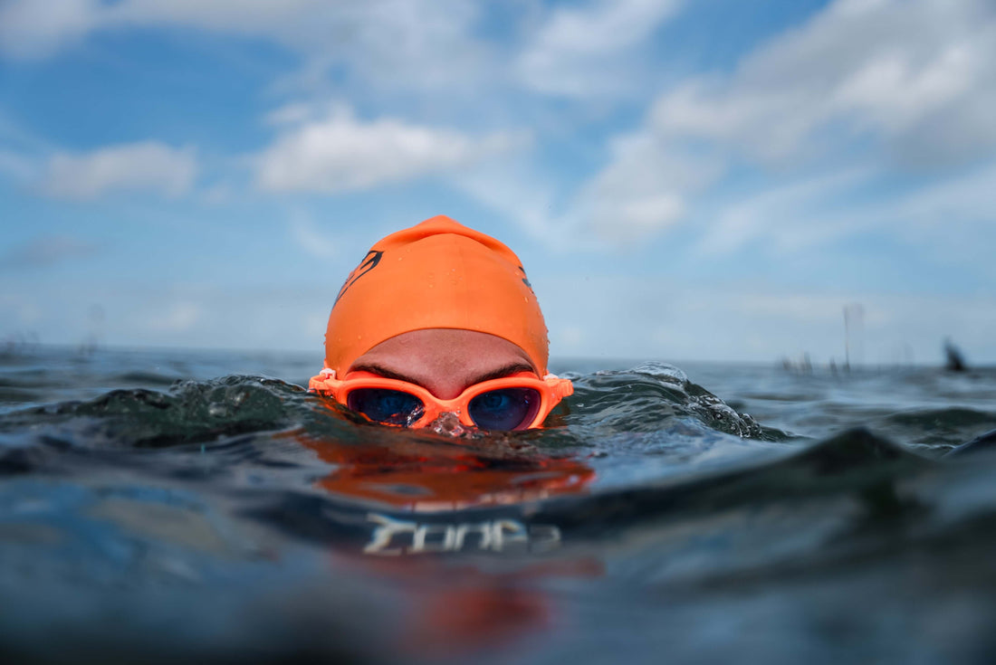 Open water swimmer with bright orange swim cap and goggles at the surface.