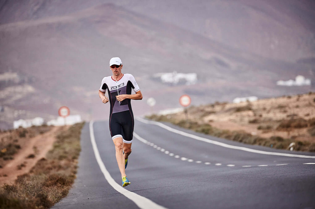 Triathlete in a Zone3 suit running on a remote desert road with mountains in the background