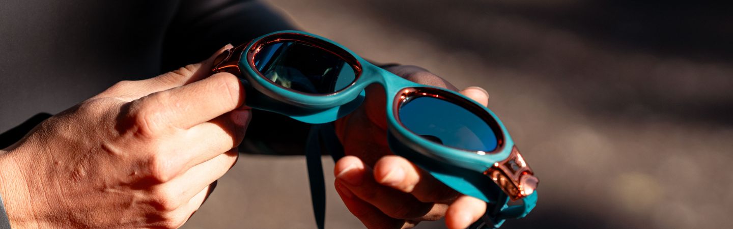 a person is holding a pair of teal Zone3 swim goggles in their hands