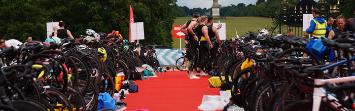 a triathlon transition showing all bikes racked on racks and lots of kit each side, all on a red carpet