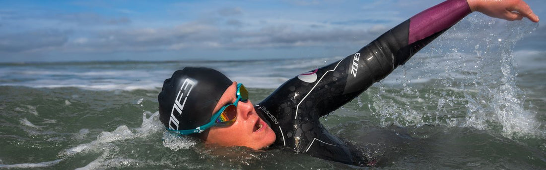 A person is swimming in the sea in a ZONE3 wetsuit and breathing to one side