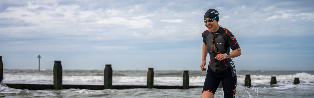 a woman is running  out of the water wearing a ZONE3 swimrun wetsuit