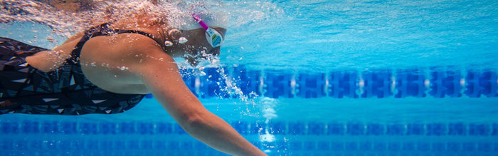 a woman is swimming in a pool doing front crawl stroke, camera is underwater perspective from side with lane ropes in shot