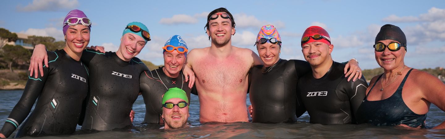 Zayd (swimming mantis coach) is surrounded by swimmers wearing wetsuits, all facing the camera. they are all in the sea.