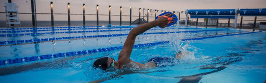 a man is swimming in a open air pool with hand paddles for training