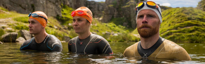 3 people are chest deep in the water all wearing zone3 wetsuits, swim caps and goggles, floating in a line