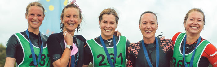 a group of women are in a line facing the camera all wearing their swimrun kit having completed a race