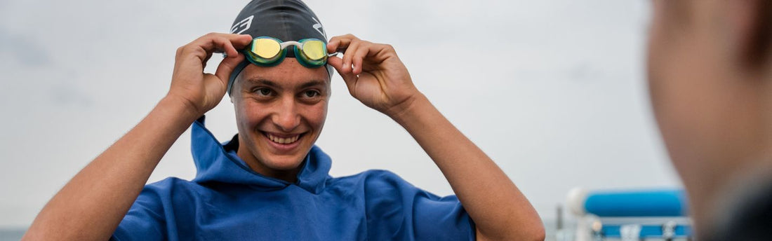 a man is wearing a zone3 swimskin with swim cap and goggles, he is facing away from camera