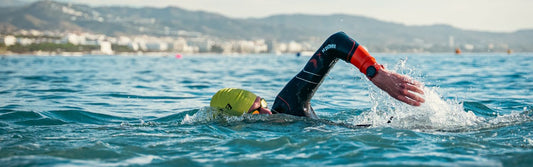 a man is swimming in the sea doing frontcrawl wearing the zone3 vanquish x wetsuit, yellow swim cap and zone3 volare goggles