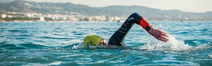a man is swimming in the sea doing frontcrawl wearing the zone3 vanquish x wetsuit, yellow swim cap and zone3 volare goggles
