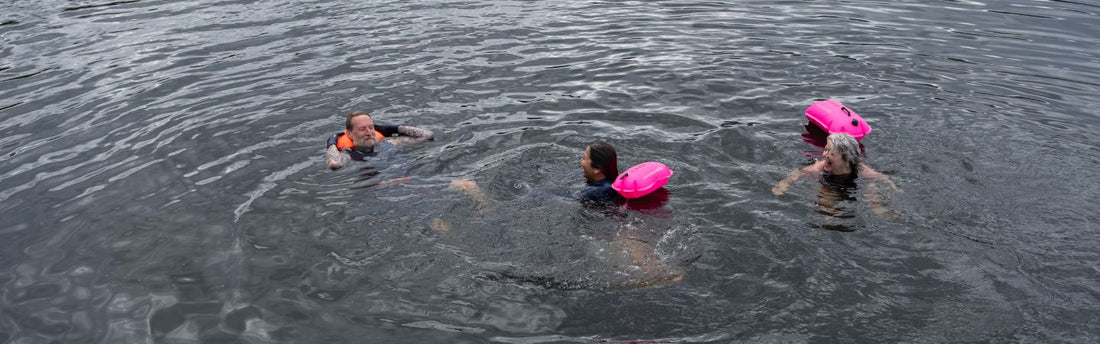 three people are floating and swimming in the open water using pink tow floats