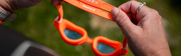 a pair of orange zone3 goggles with blie tinted lense is being held - the photo is a close up of the goggles
