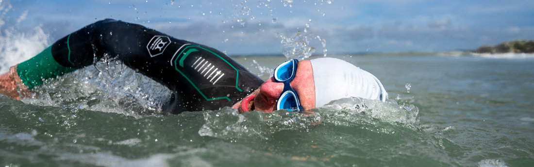 a man is swimming in the open water breathing to one side with swim goggles facing the camera