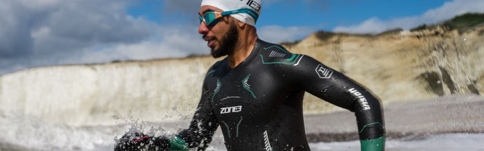 a man is running into the ocean wearing a ZONE3 Vision Wetsuit, cap and goggles