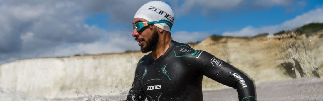 a man is running in the water at the beach wearing a ZONE3 swim wetsuit