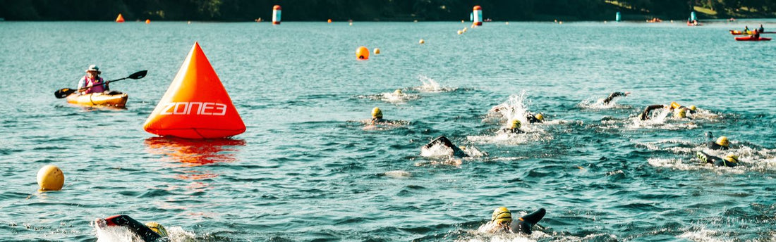 a group of people are swimming in the open water event, with  a buoy in the water to turn around
