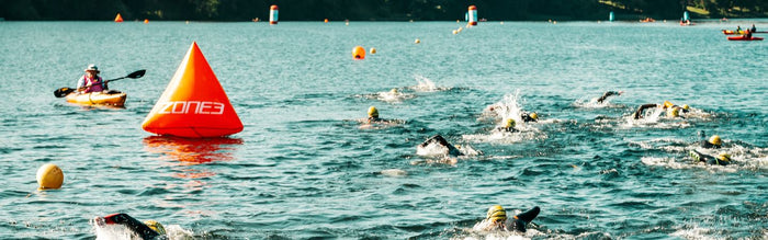 a group of people are swimming in the open water event, with  a buoy in the water to turn around