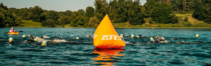 a zone3 buoy is in the lake with swimmer swimming around it the buoy is orange