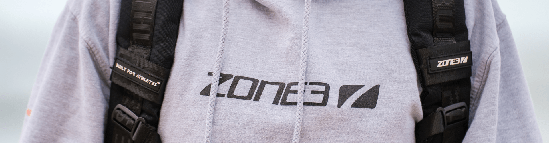 Athlete wearing a light gray Zone3 hoodie with black backpack straps and branding.