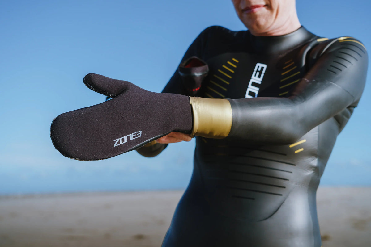 A swimmer's hands in black ZONE3 neoprene gloves holding a pink tow float.