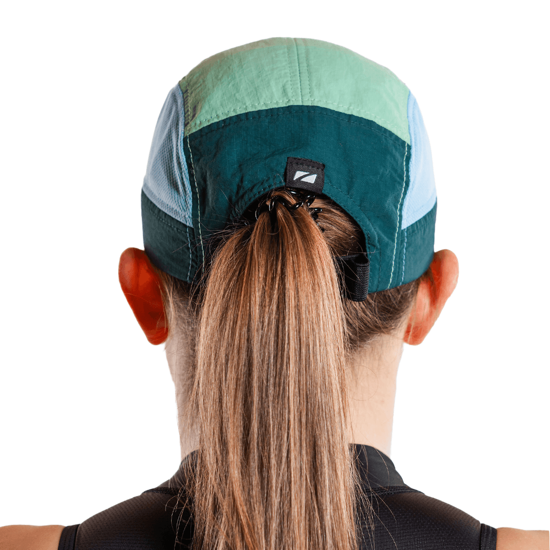 Blaugrüne 5-Panel-Laufkappe, getragen von einer Person mit Pferdeschwanz auf weißem Hintergrund