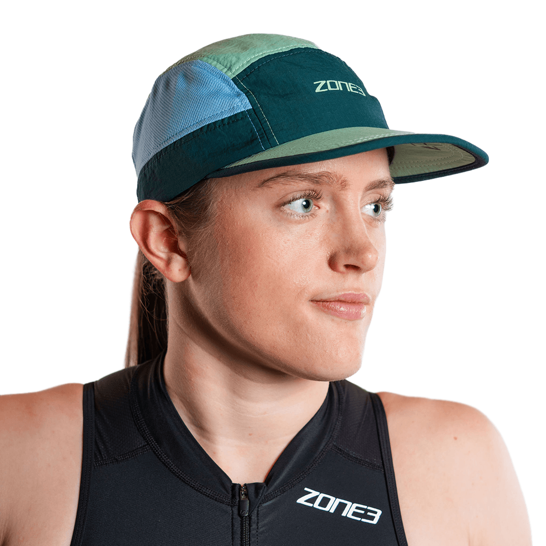 Person, die eine blaugrüne 5-Panel-Laufkappe mit Zone3-Logo auf weißem Hintergrund trägt