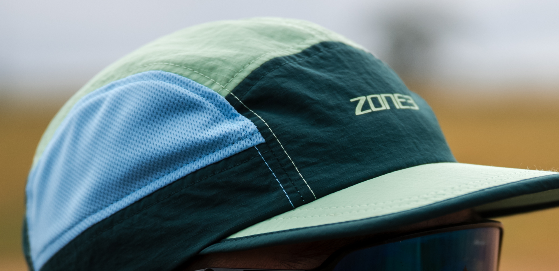 Close-up of a person wearing a zone3 5 panel multicolored running cap with a zone3 logo against a blurred background