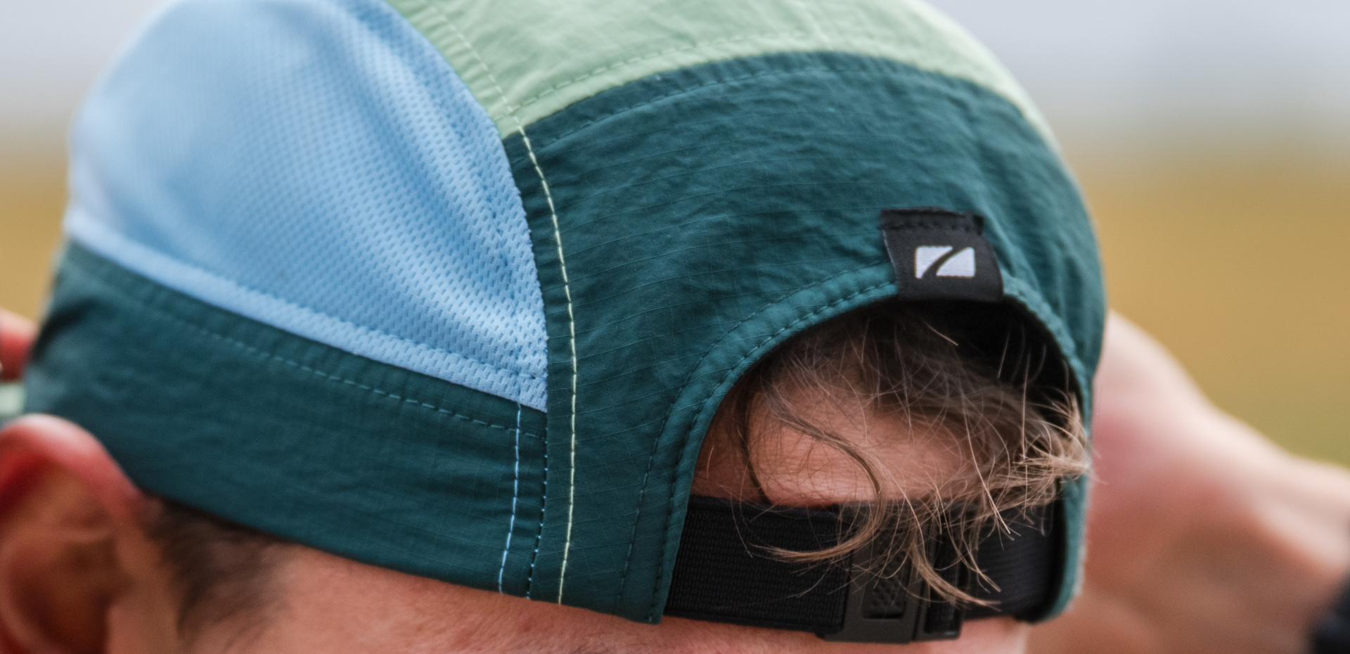 Close-up of a person wearing a zone3 5 panel multicolored running cap with a zone3 logo.