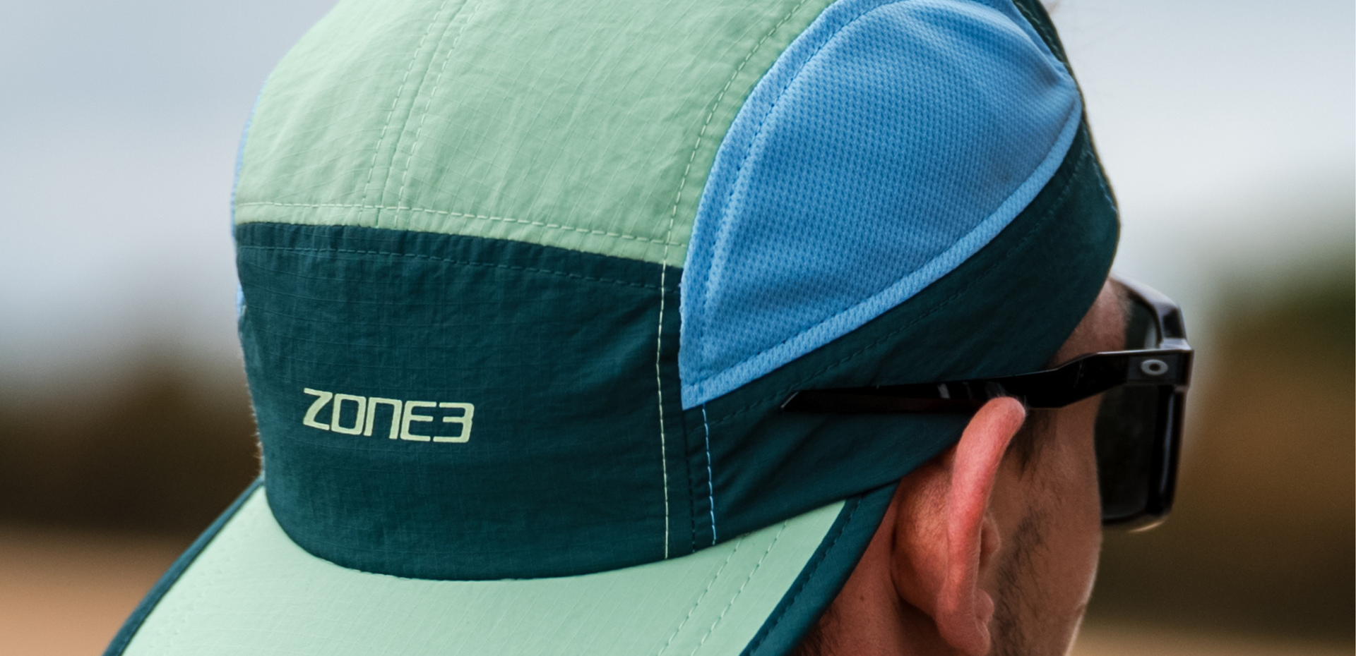 Person wearing a Zone3 5 panel running cap and sunglasses with a blurred background