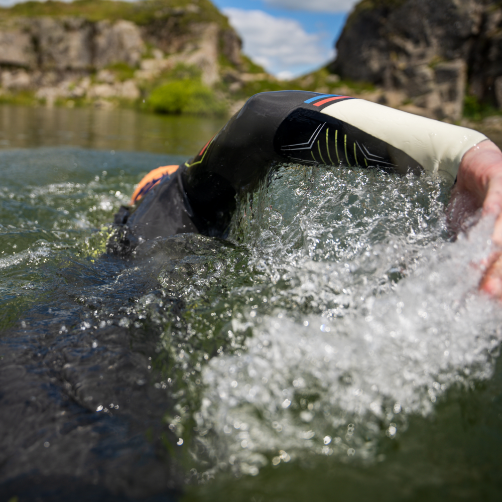 Person swimming in a ZONE3 Aspire wetsuit in open water. The person is in front-crawl with their head under the water and right hand emerging from the water to complete the stroke.