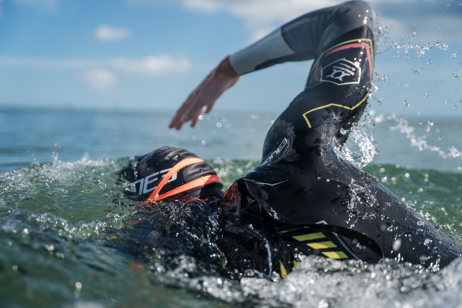 Person swimming in the sea. Wearing a ZONE3 wetsuit, black swim cap and orange goggles