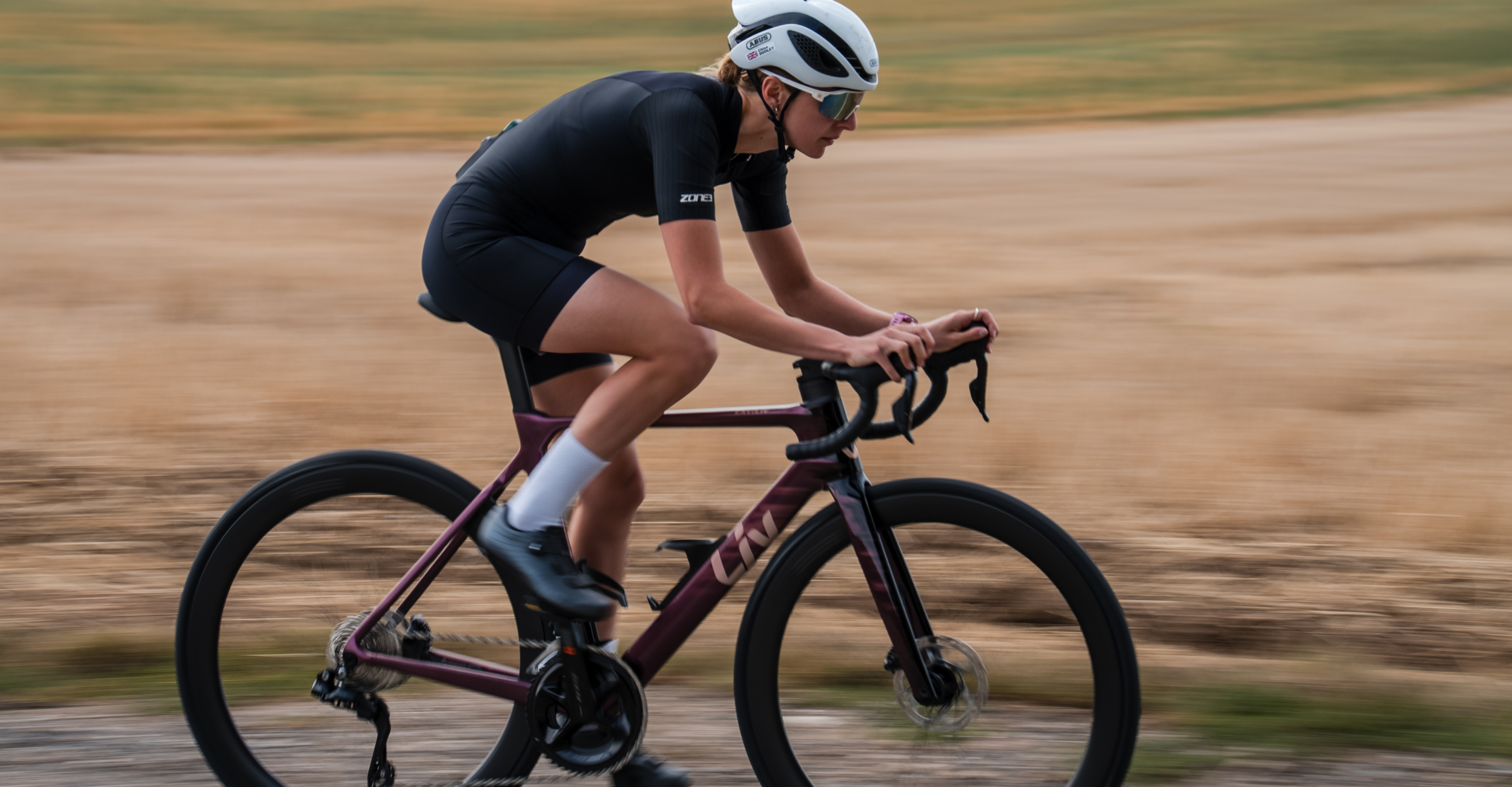 Person wearing black zone3 trisuit riding a bicycle on a road with a blurred background