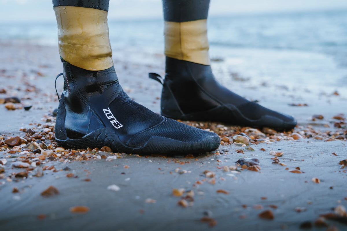 close up of the bottom of the Zone3 thermal wetsuit paired with the Zone3 thermal socks at the beach. 