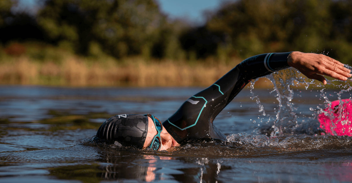 Athlete wearing the Zone3 Advance wetsuit in open water while swimming. athlete paired the wetsuit with Zone3 black swim cap and teal goggles. 