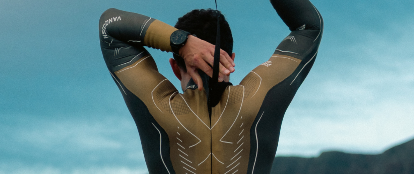 Athlete wearing a ZONE3 Vanquish X Gold wetsuit. He is facing away with both hands in use adjusting the rear neck of the wetsuit.