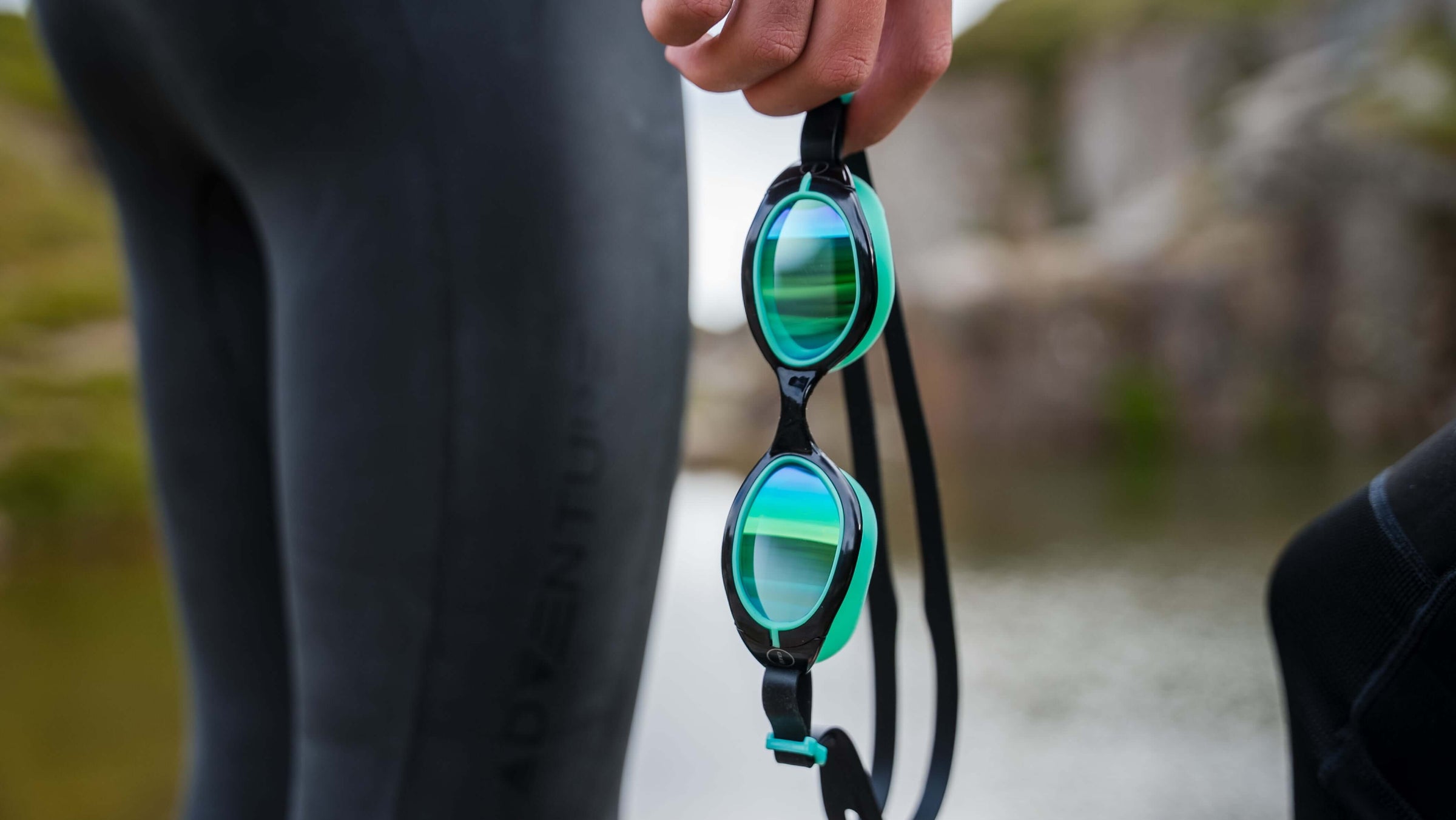 Person holding a pair of green Aquahero Goggles swim goggles with a blurred natural background