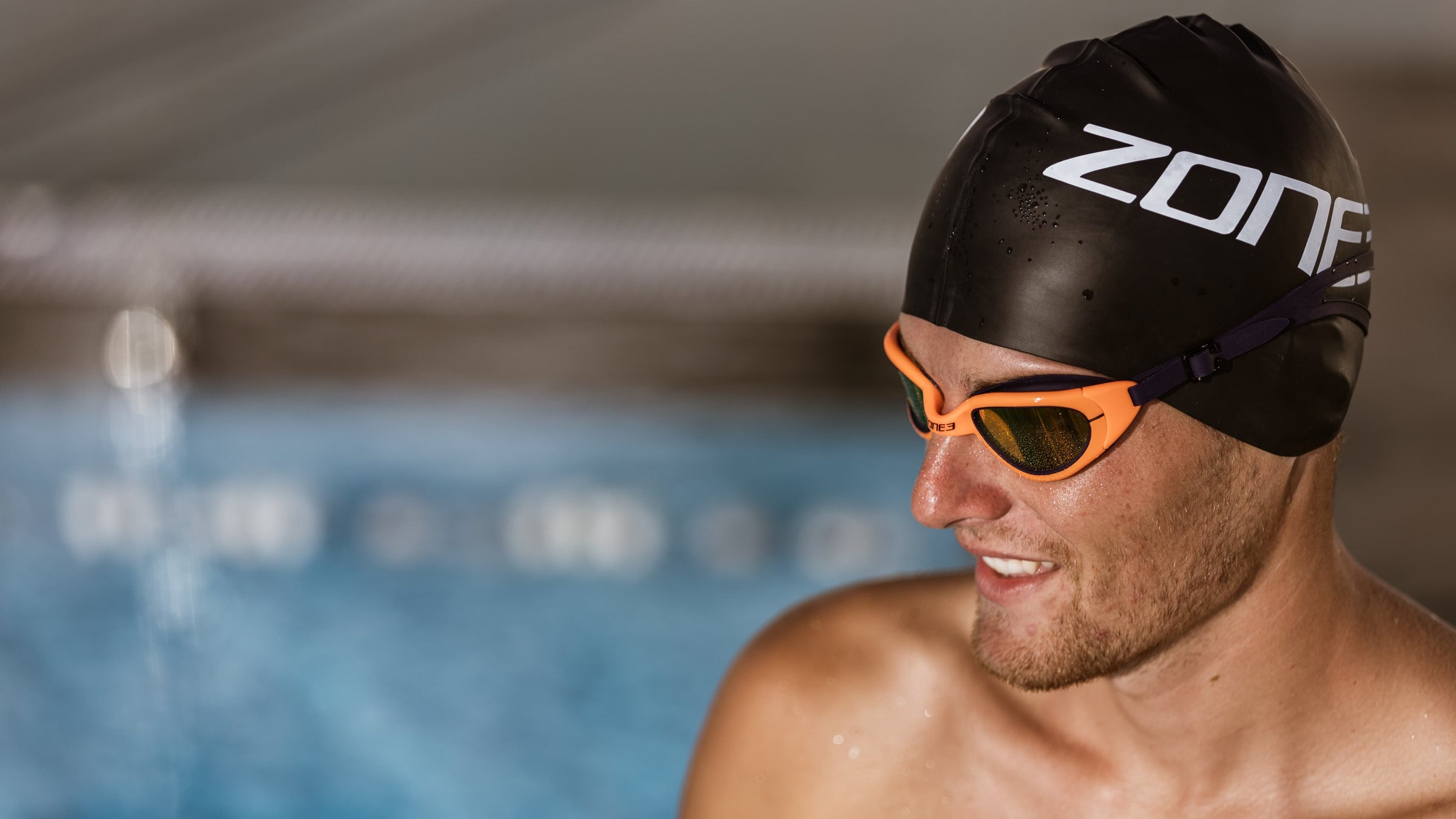 Man wearing a Zone3 black swim cap and attack Navy/Neon Orange
 goggles