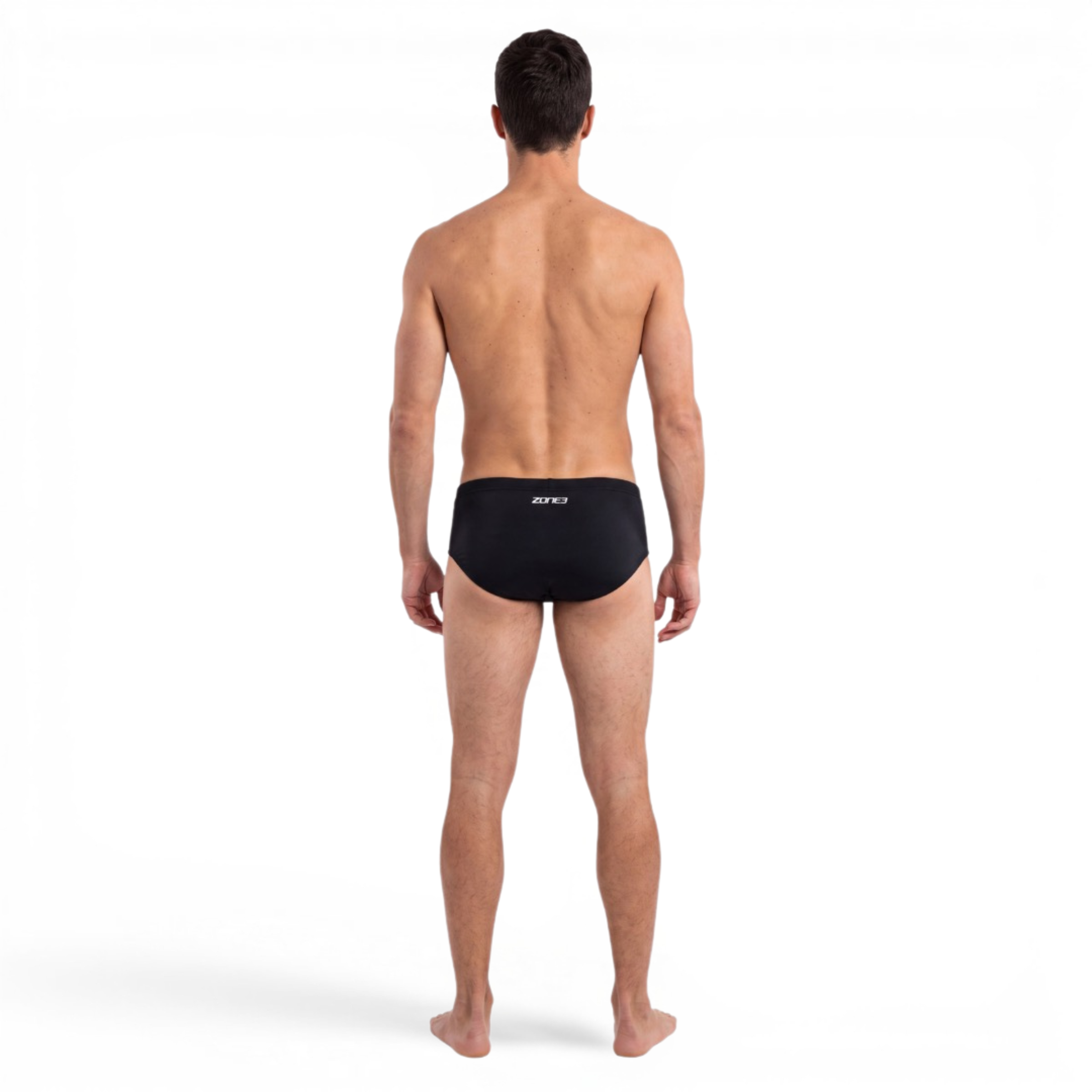 A man viewed from the back wearing black swim briefs with a small white logo on the back waistband, standing against a plain white studio background.
