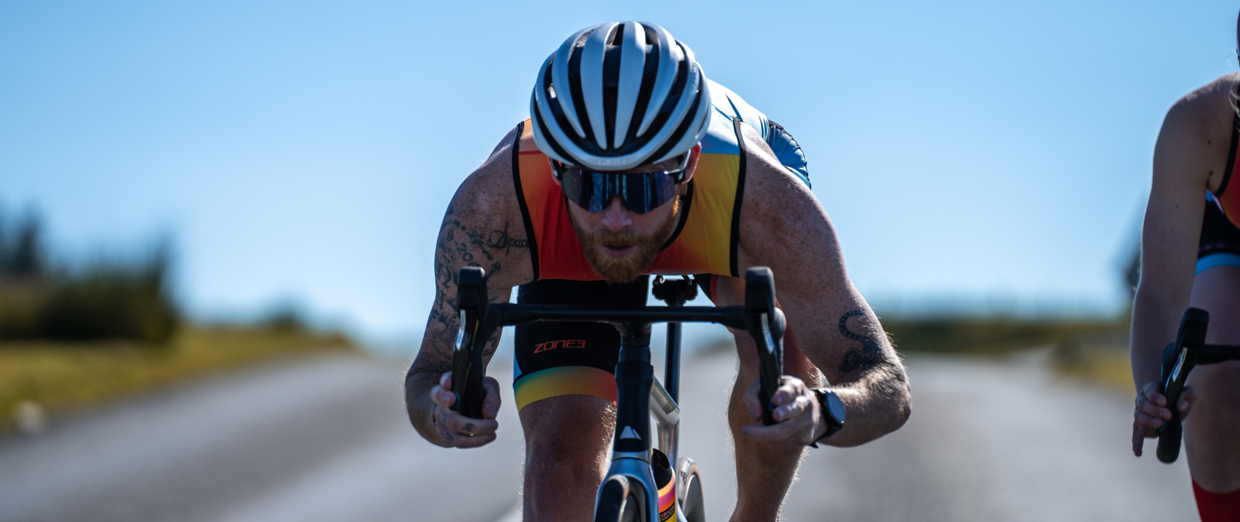 Man wearing a ZONE3 Activate plus trisuit on a bike. He is leaning forward towards the bars of the bike and looking forward.
