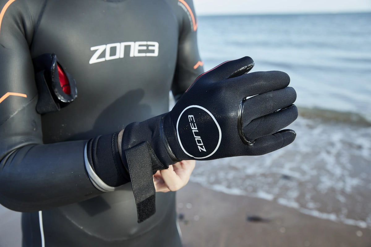 Athlete putting on his Zone3 heat tech gloves at the beach before an open water swim. 