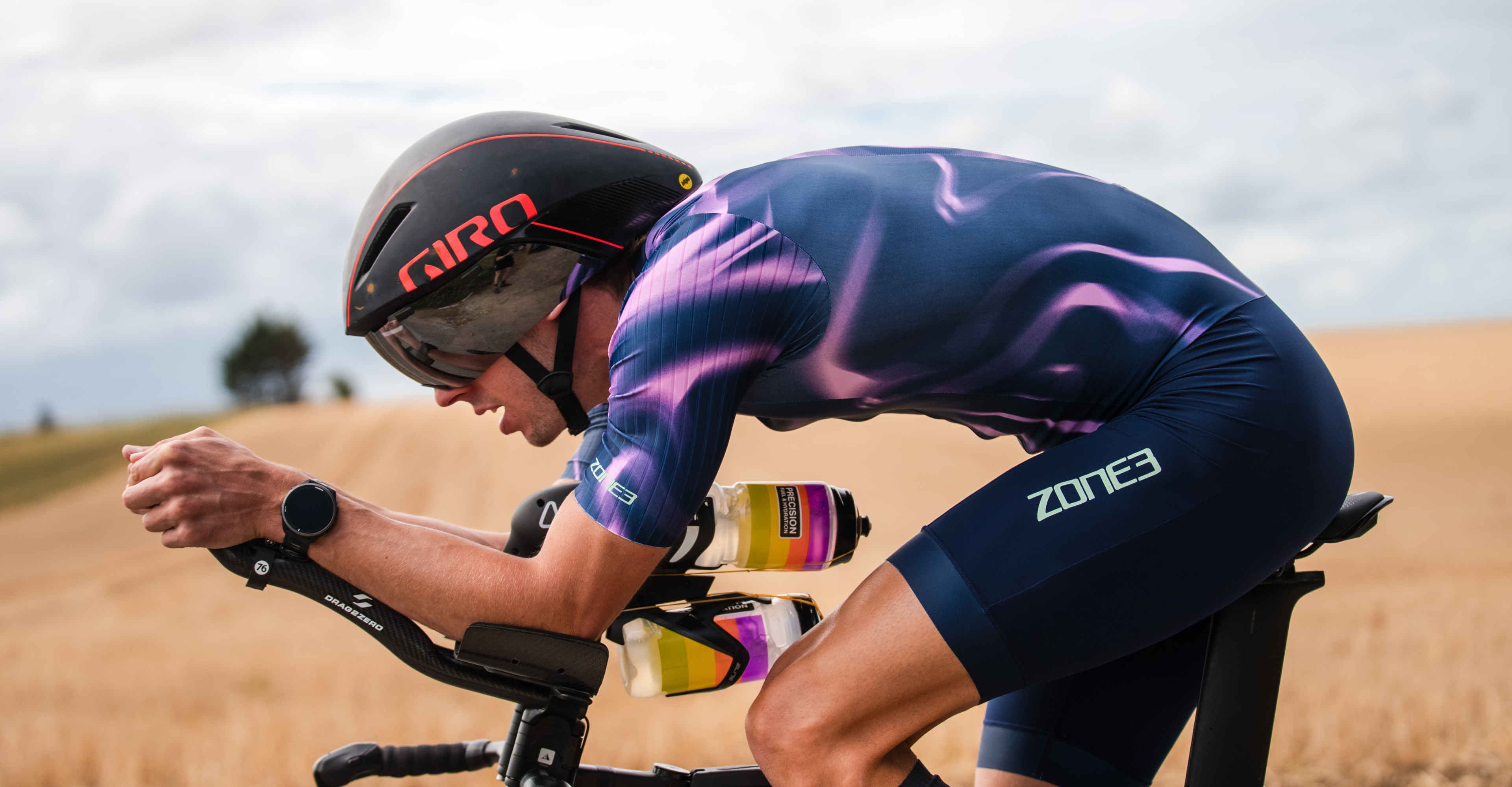 Man crying in a colourful Zone3 Trisuit and cap with dry grass field landscape in the background