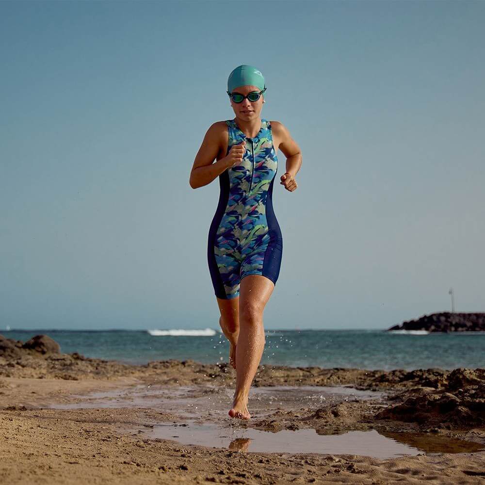 Junior running Wearing the Zone3 print Trisuit at the beach with teal swimcap and goggles. 
