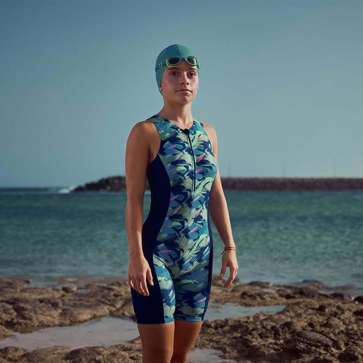 Junior Wearing the Zone3 print Trisuit at the beach with teal swimcap and goggles. 